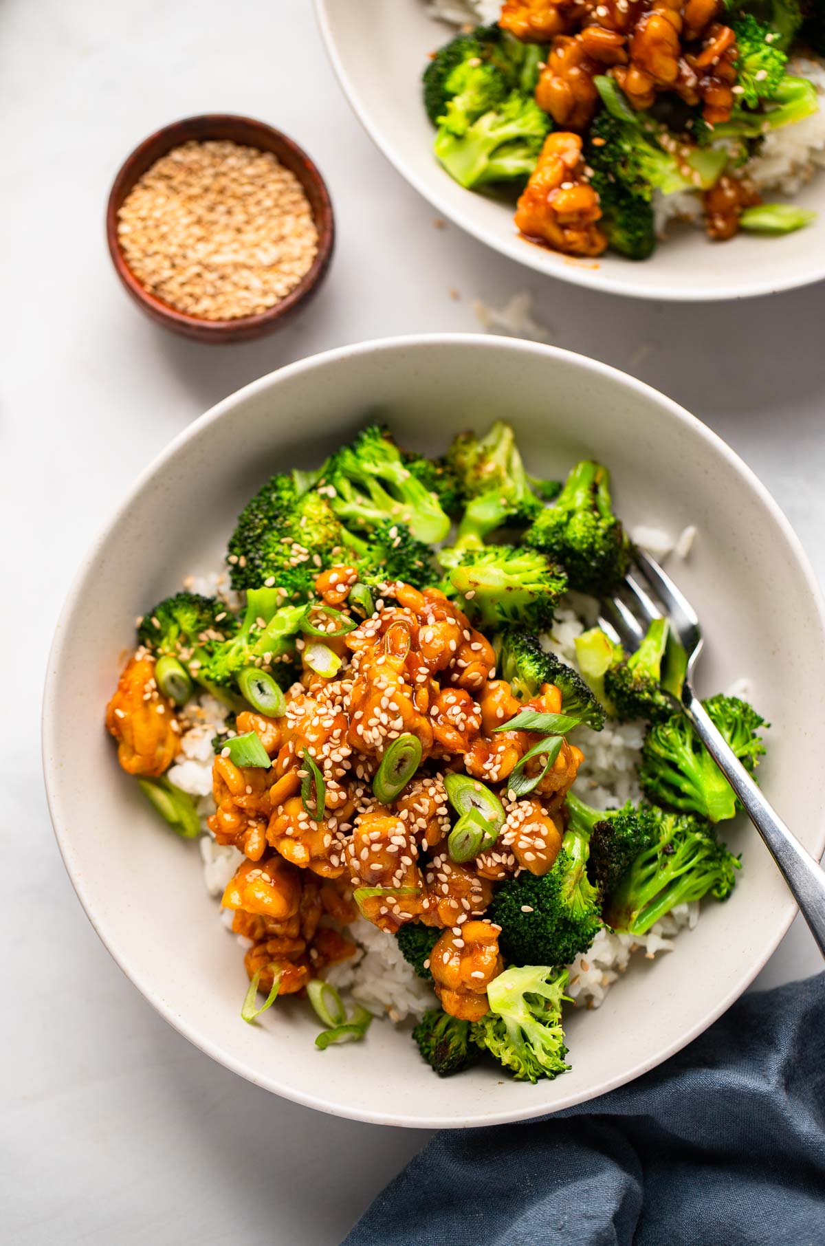 sticky tempeh in a bowl with rice and broccoli topped with green onion and sesame seeds. 