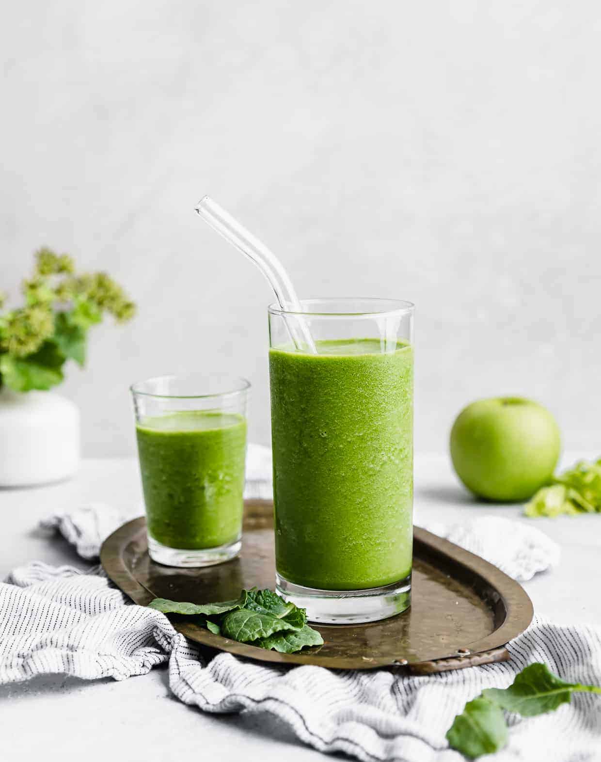 celery smoothie in a tall glass with a glass straw.