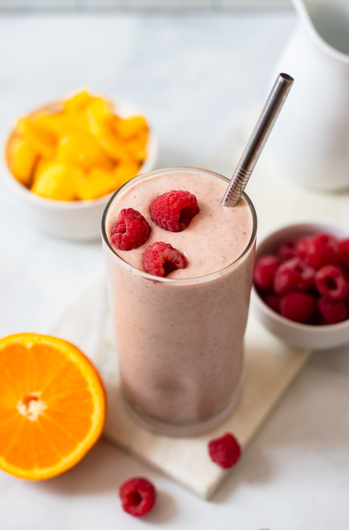 mango raspberry smoothie in a tall glass garnished with fresh berries. 