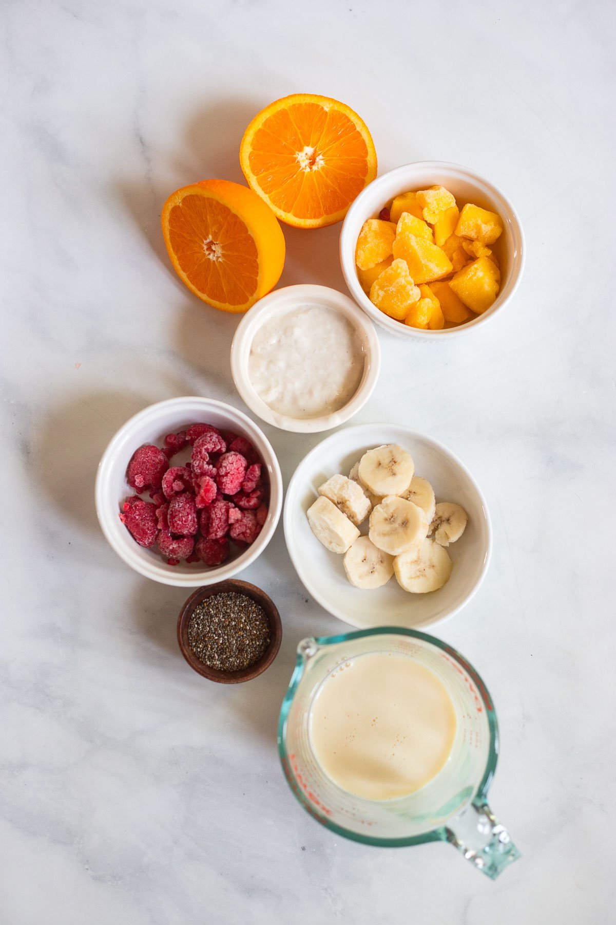 mango raspberry smoothie ingredients in small bowls on a white background. 