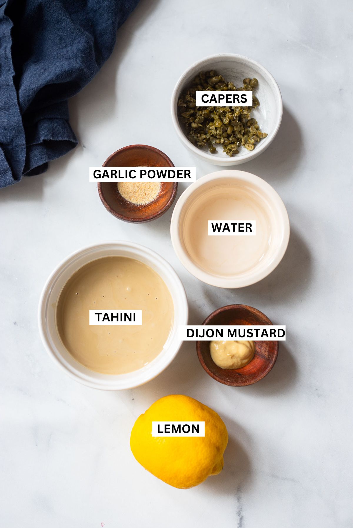 Tahini Caesar dressing ingredients in small dishes with text labels. 