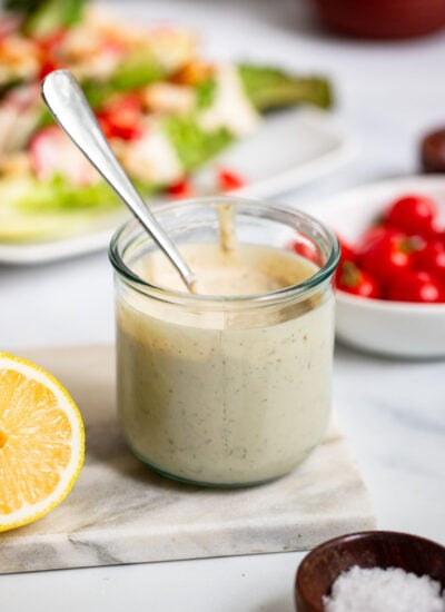 Tahini Caesar dressing in a glass jar with a spoon for serving.