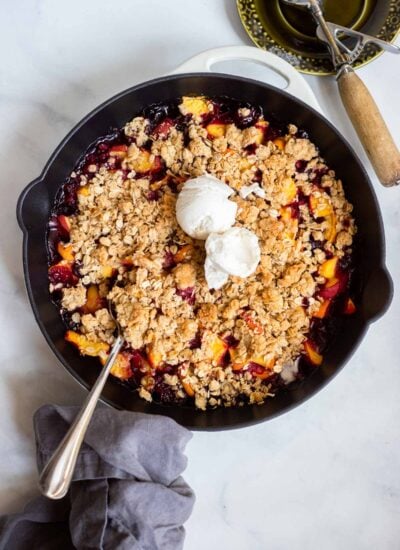 baked peach blueberry crisp in skillet topped with ice cream.