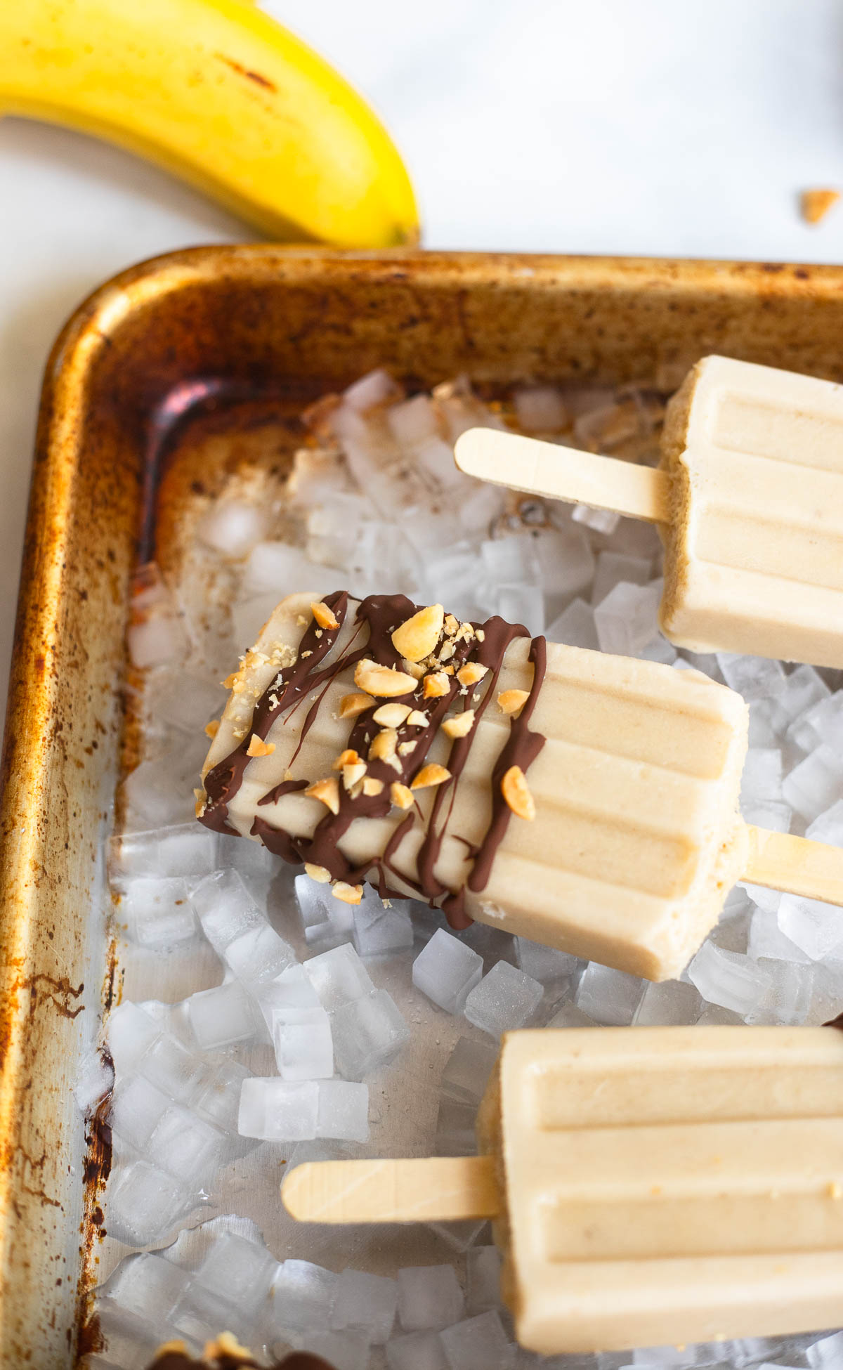 close up photo of banana popsicle with chocolate and chopped peanuts.