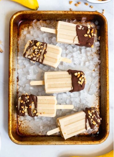peanut butter banana popsicles dipped in chocolate on a metal tray.