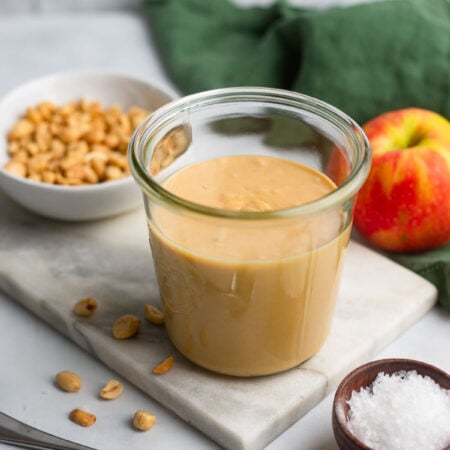 homemade peanut butter in a glass jar next to an apple.