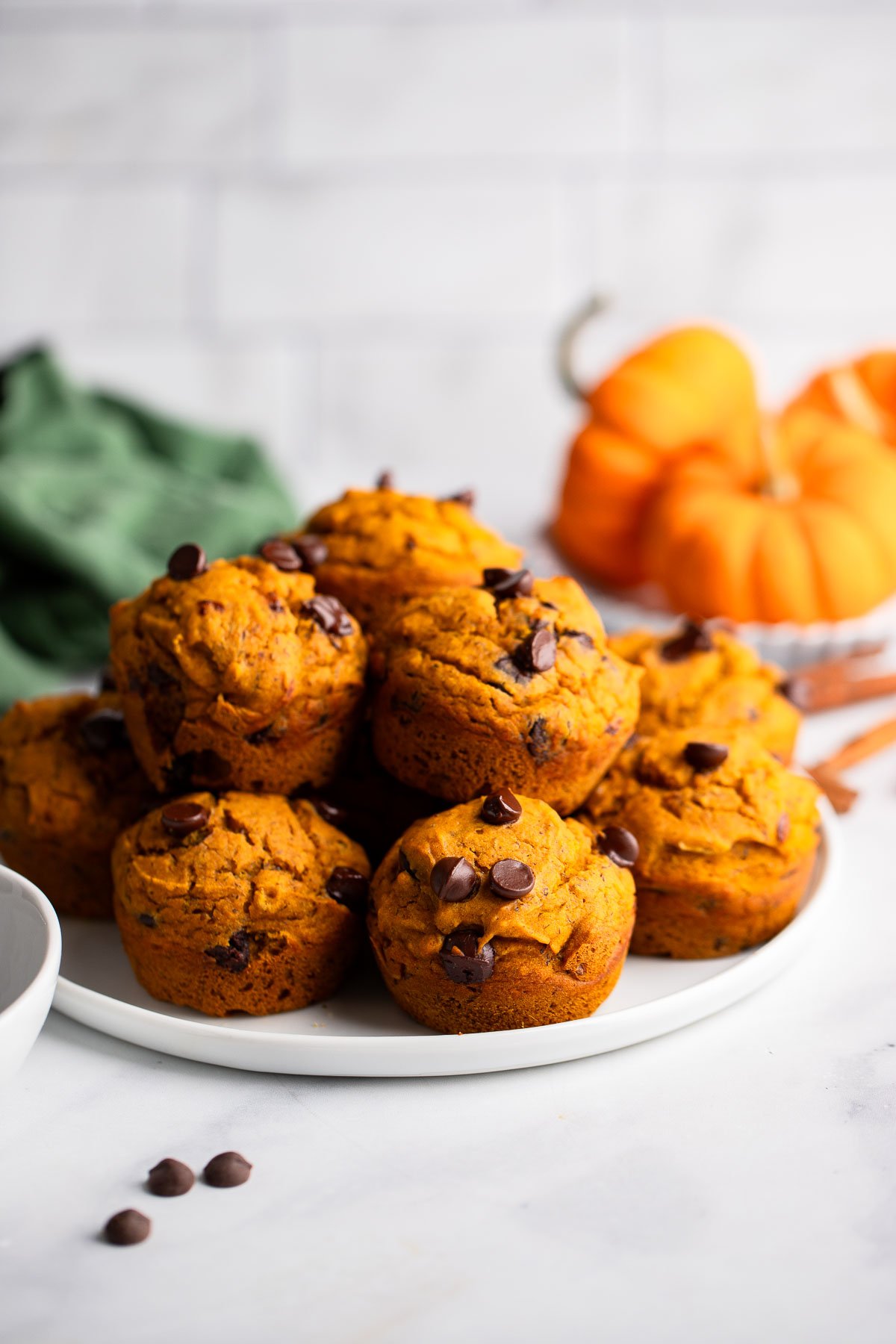 vegan pumpkin chocolate chips muffins piled onto a white plate. 