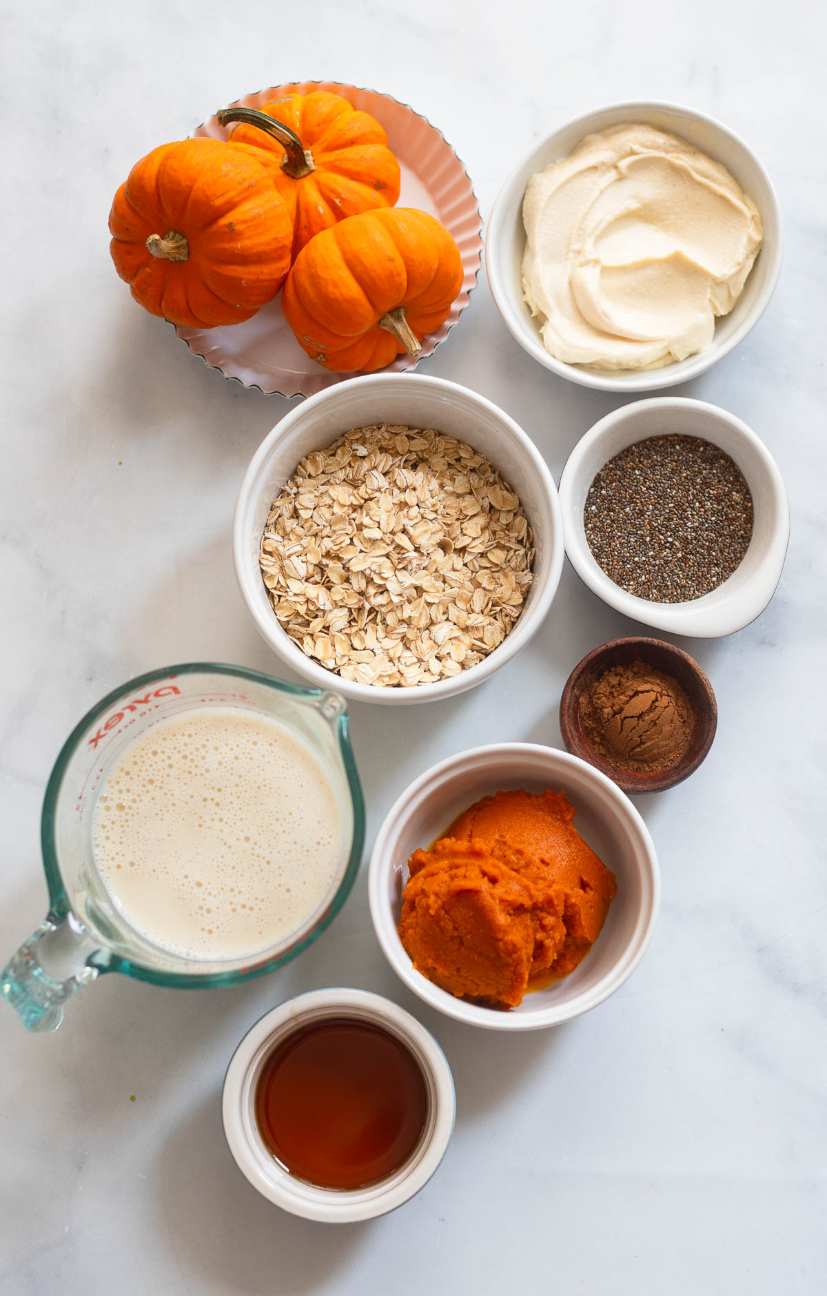 pumpkin pie overnight oats ingredients in small bowls on a white background.