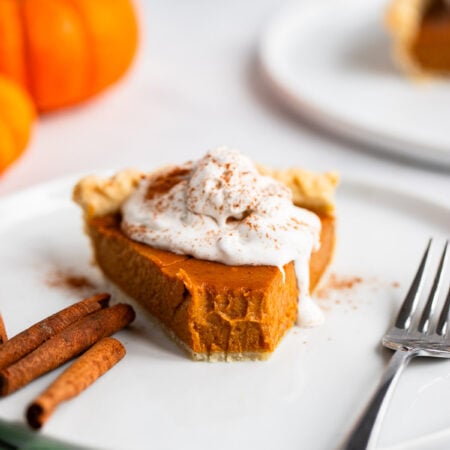 slice of vegan pumpkin pie on a plate topped with whipped cream.