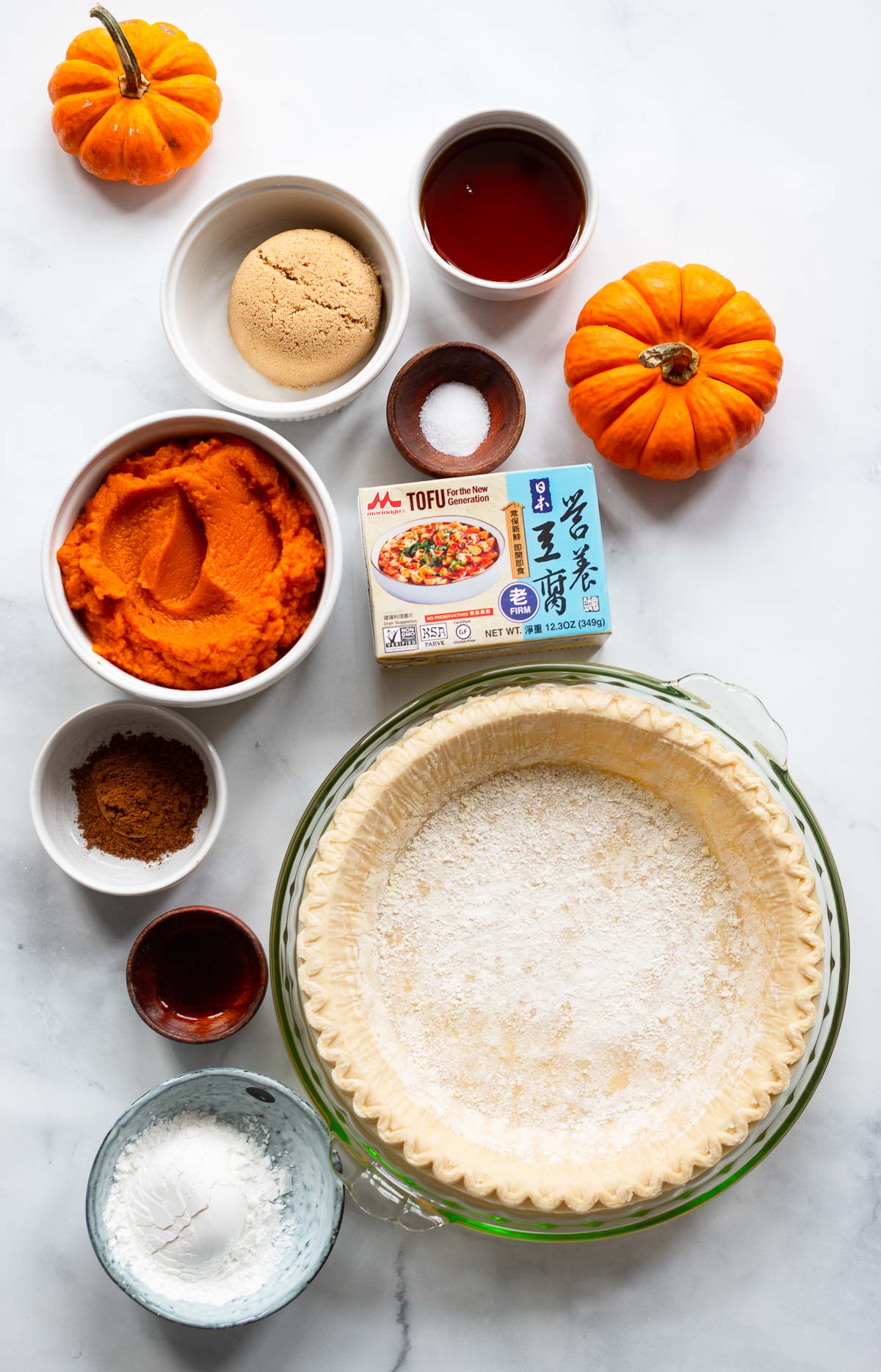 pumpkin pie ingredients in small bowls laid out on a white background.