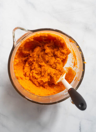 mashed sweet potatoes in an upright mixer bowl with a spatula. 