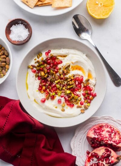 vegan whipped feta dip in a serving bowl topped with pomegranate and pistachios.