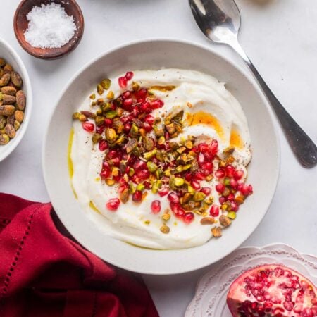 vegan whipped feta dip in a serving bowl topped with pomegranate and pistachios.