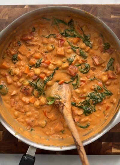 sweet potato peanut curry in a skillet with a wooden spoon.