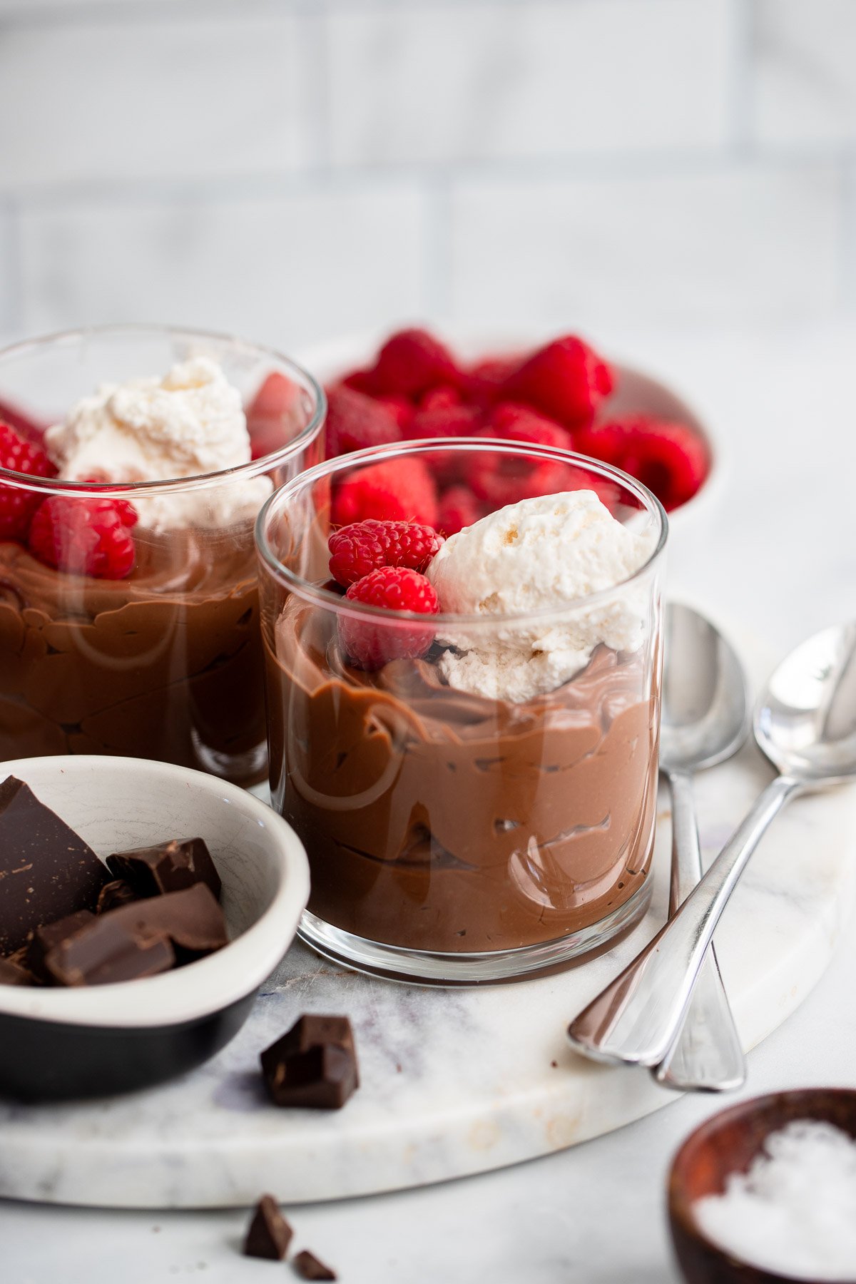 vegan chocolate mousse in glasses topped with whipped cream and fresh raspberries. 