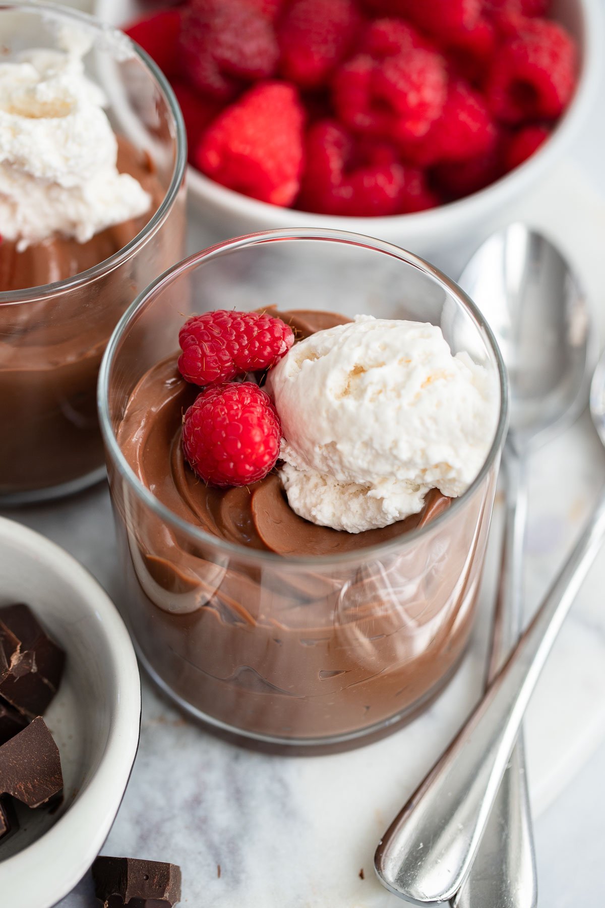 chocolate tofu mousse in a glass topped with whipped cream and fresh raspberries. 
