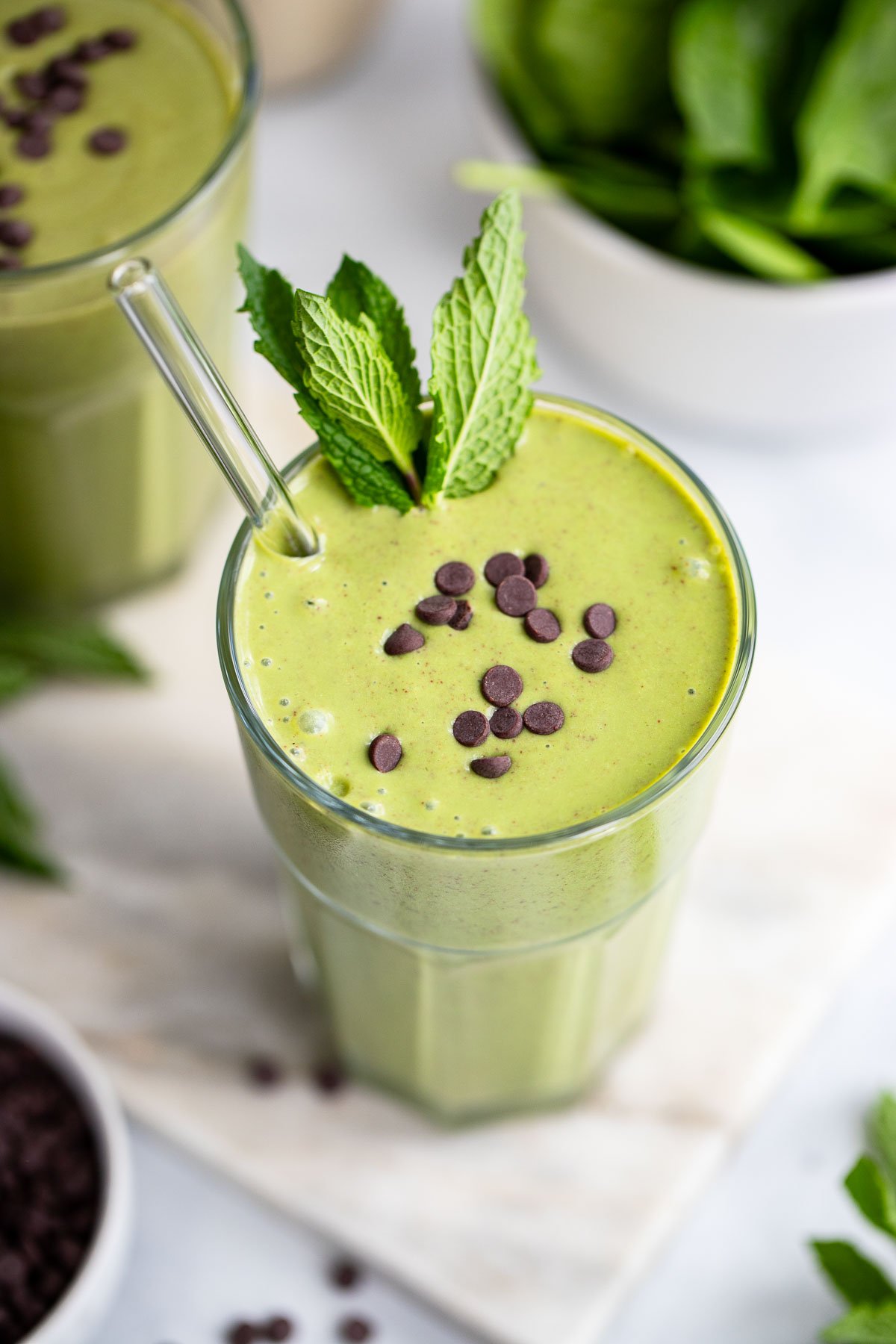 mint smoothie in a tall glass with a glass straw. 