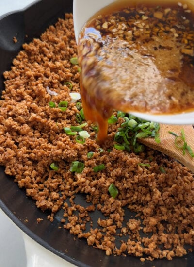 sauce pouring into skillet with cooked vegan ground beef. 