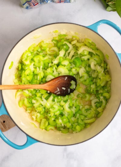 celery and onions sautéed in a dutch oven with a wooden spoon.