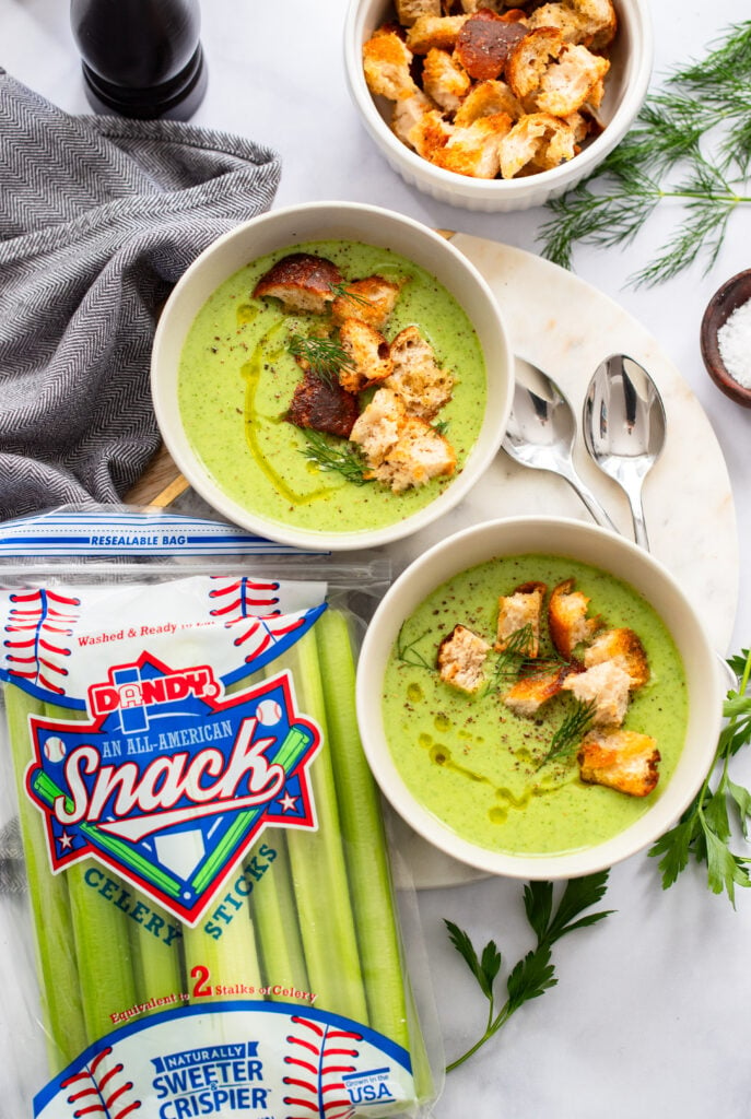 two bowls of creamy celery soup garnished with croutons on a white background. 