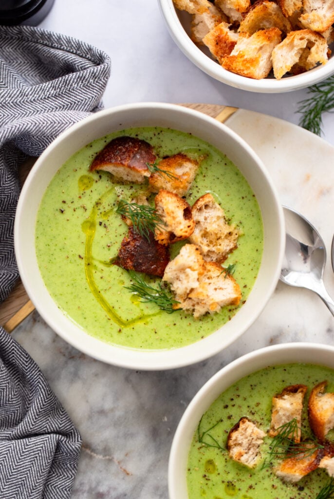 bowl of creamy celery soup topped with croutons and fresh dill on a white background. 