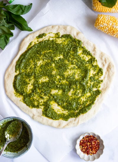pesto spread in an even layer on raw pizza crust. 