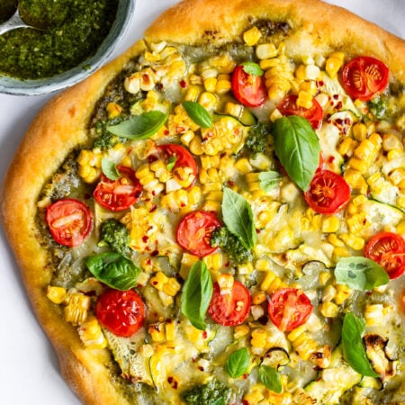 uncut sweet corn pizza garnished with fresh basil leaves on a white background.