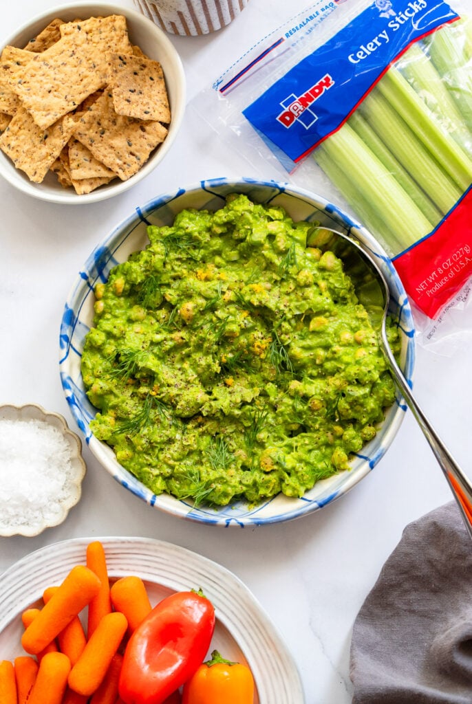 green goddess chickpea salad in a bowl next to crackers and celery sticks.