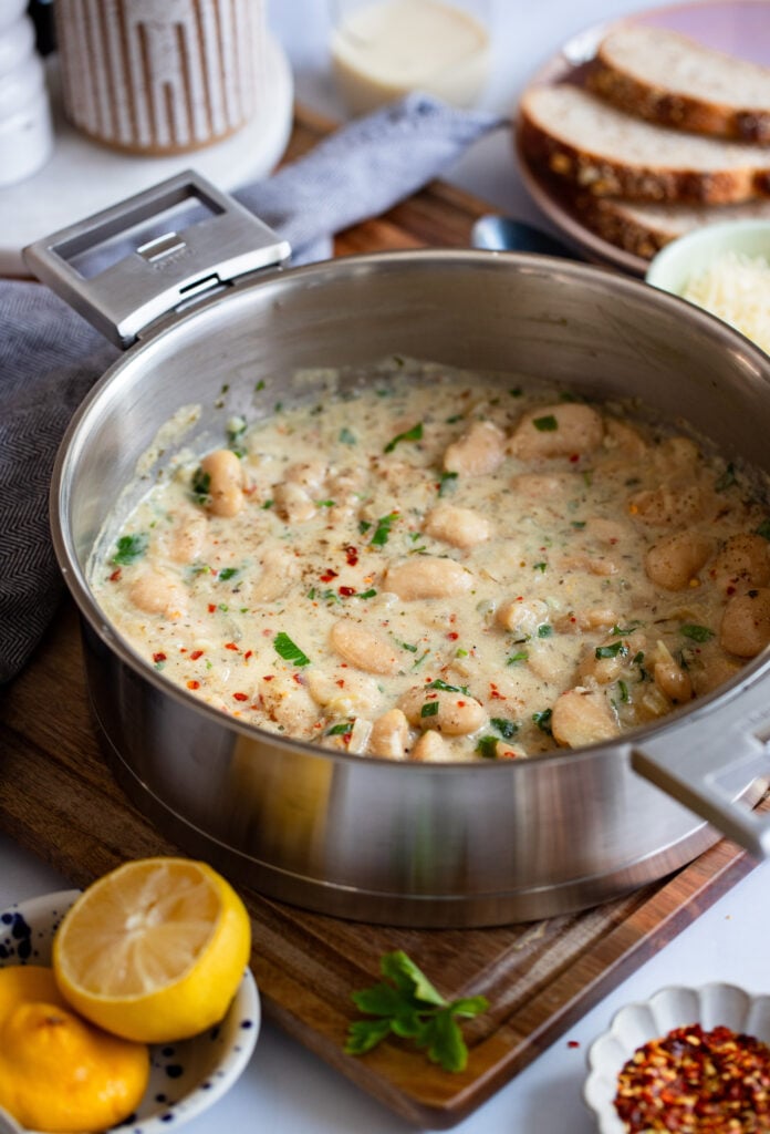 creamy parmesan butter bean sin a skillet with fresh bread and lemon on the table.