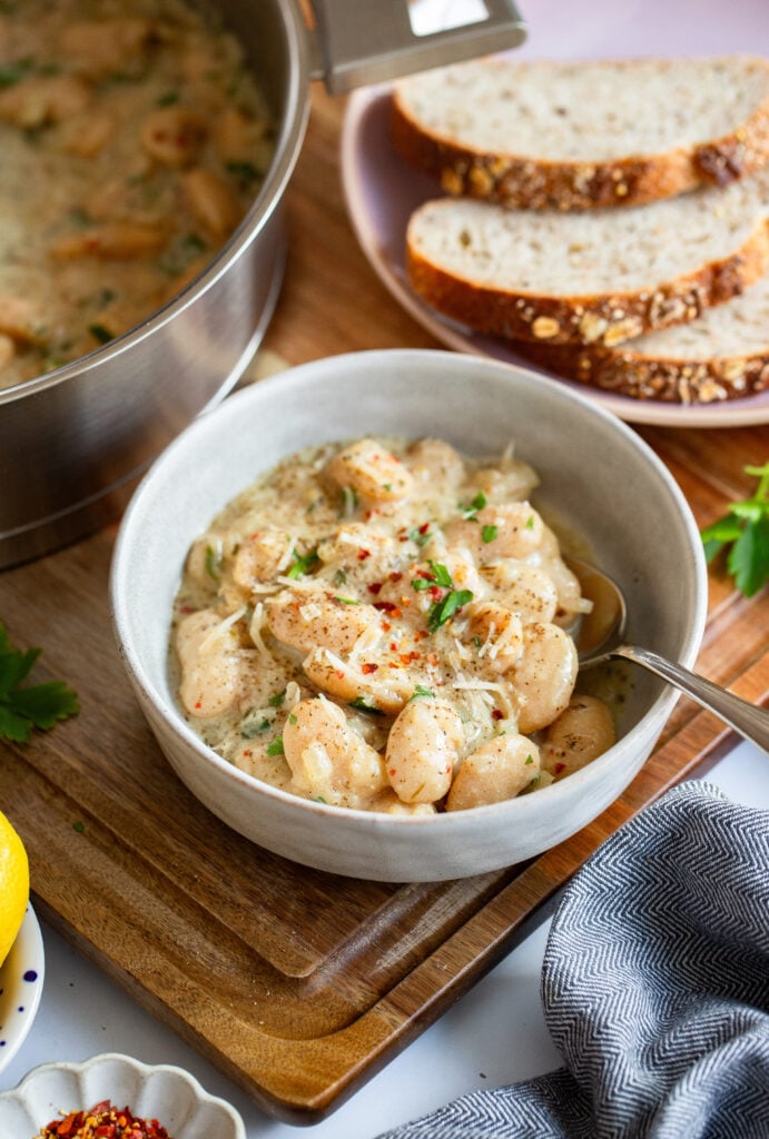 creamy parmesan beans in bowl garnished with parmesan and parsley.