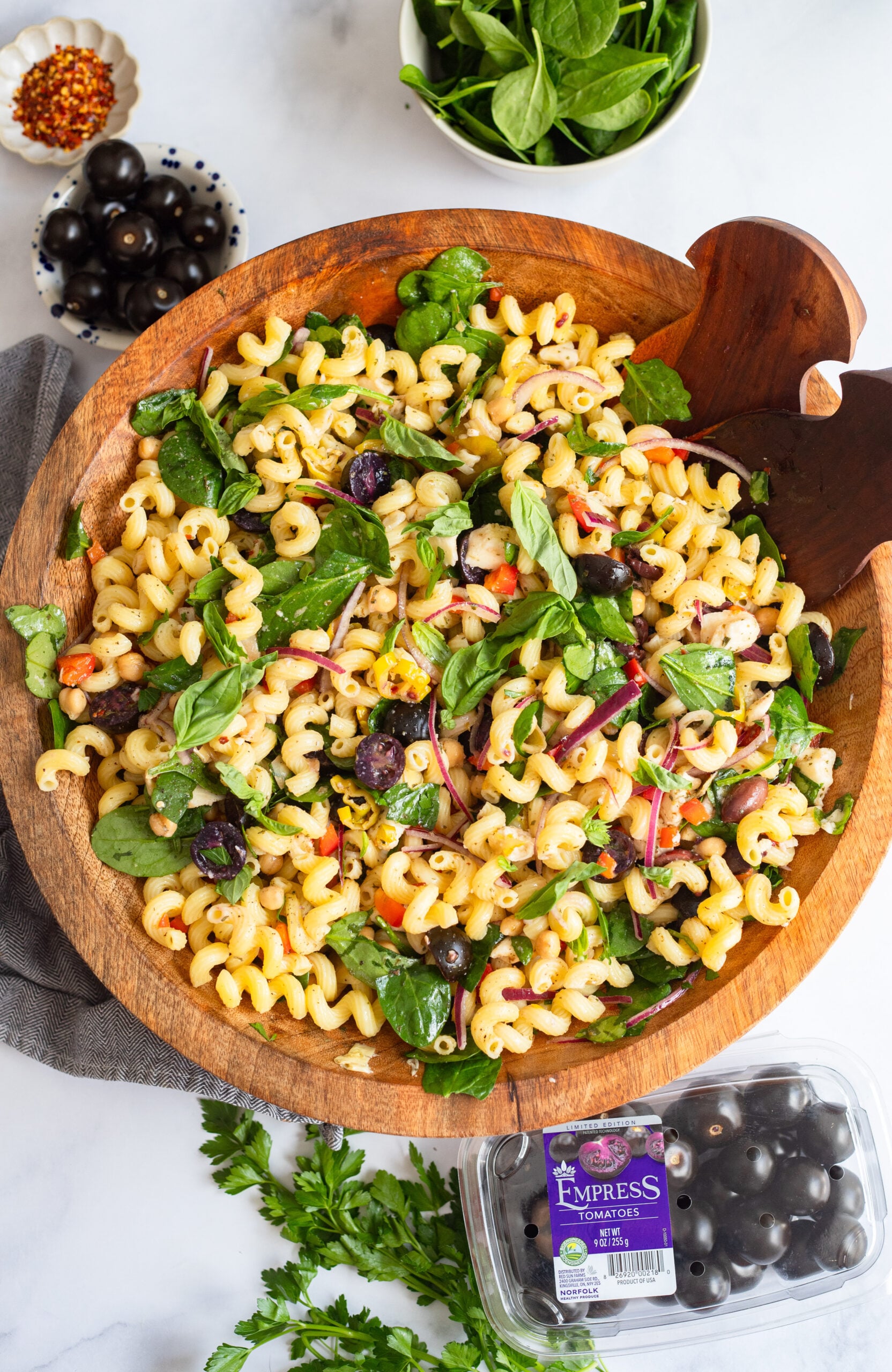 Mediterranean pasta salad in a large wooden bowl garnished with fresh basil. 