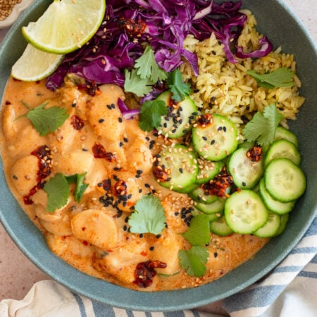 peanut sauce butter beans in a bowl with rice, cucumbers. and purple cabbage