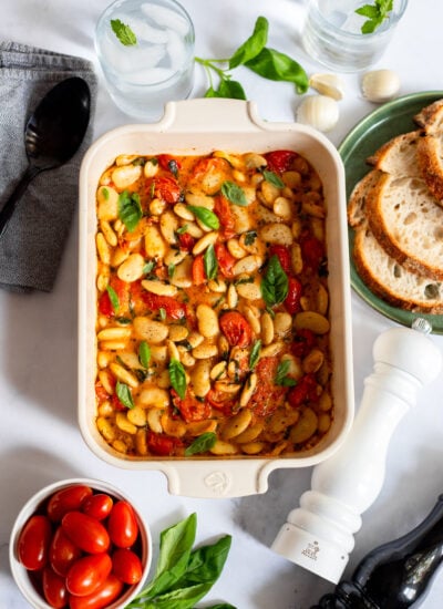 baked feta butter beans with tomatoes and basil in a ceramic baking dish
