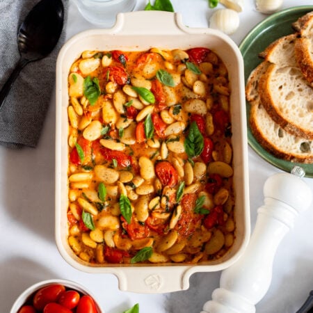 baked feta butter beans with tomatoes and basil in a ceramic baking dish