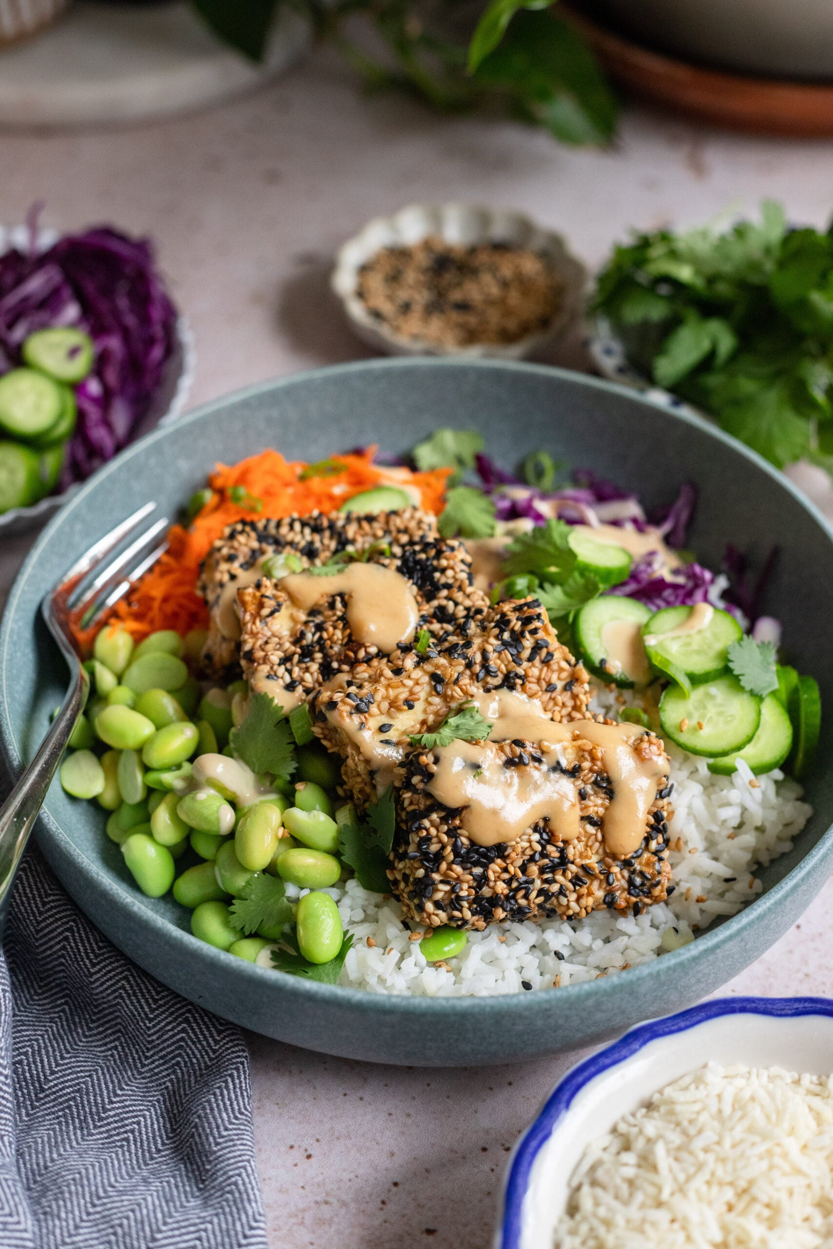 sesame crusted tofu in a bowl with tahini sauce, rice, and colorful veggies