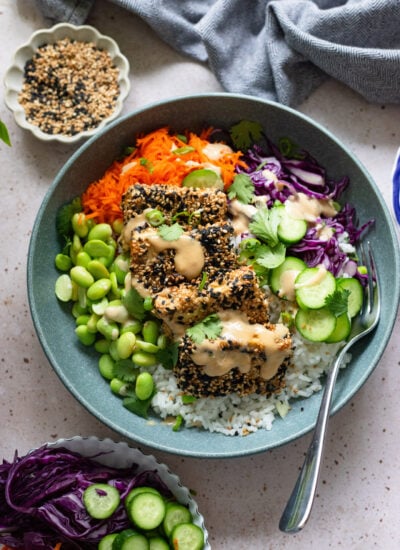 sesame crusted tofu bowl with fresh veggies and tahini sauce in a blue bowl