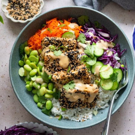 sesame crusted tofu bowl with fresh veggies and tahini sauce in a blue bowl