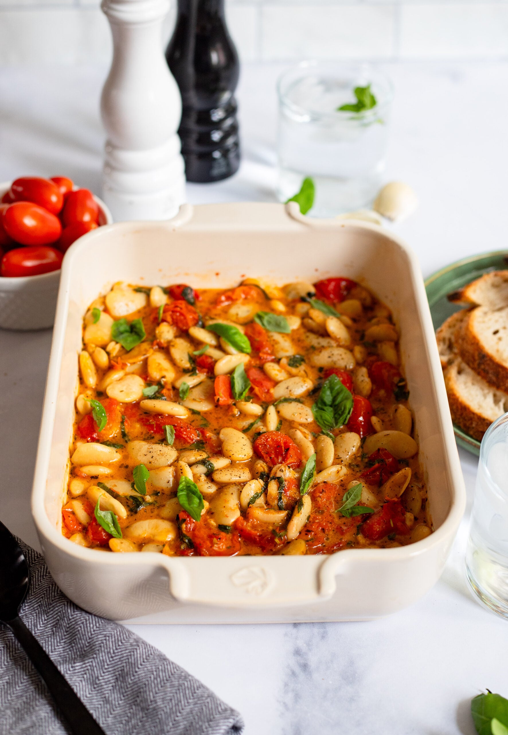 baked feta butter beans with tomato and basil in a ceramic baking dish.