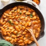 saucy butter beans in an enamelware skillet with a spoon