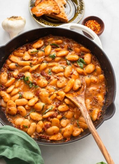 saucy butter beans in an enamelware skillet with a spoon