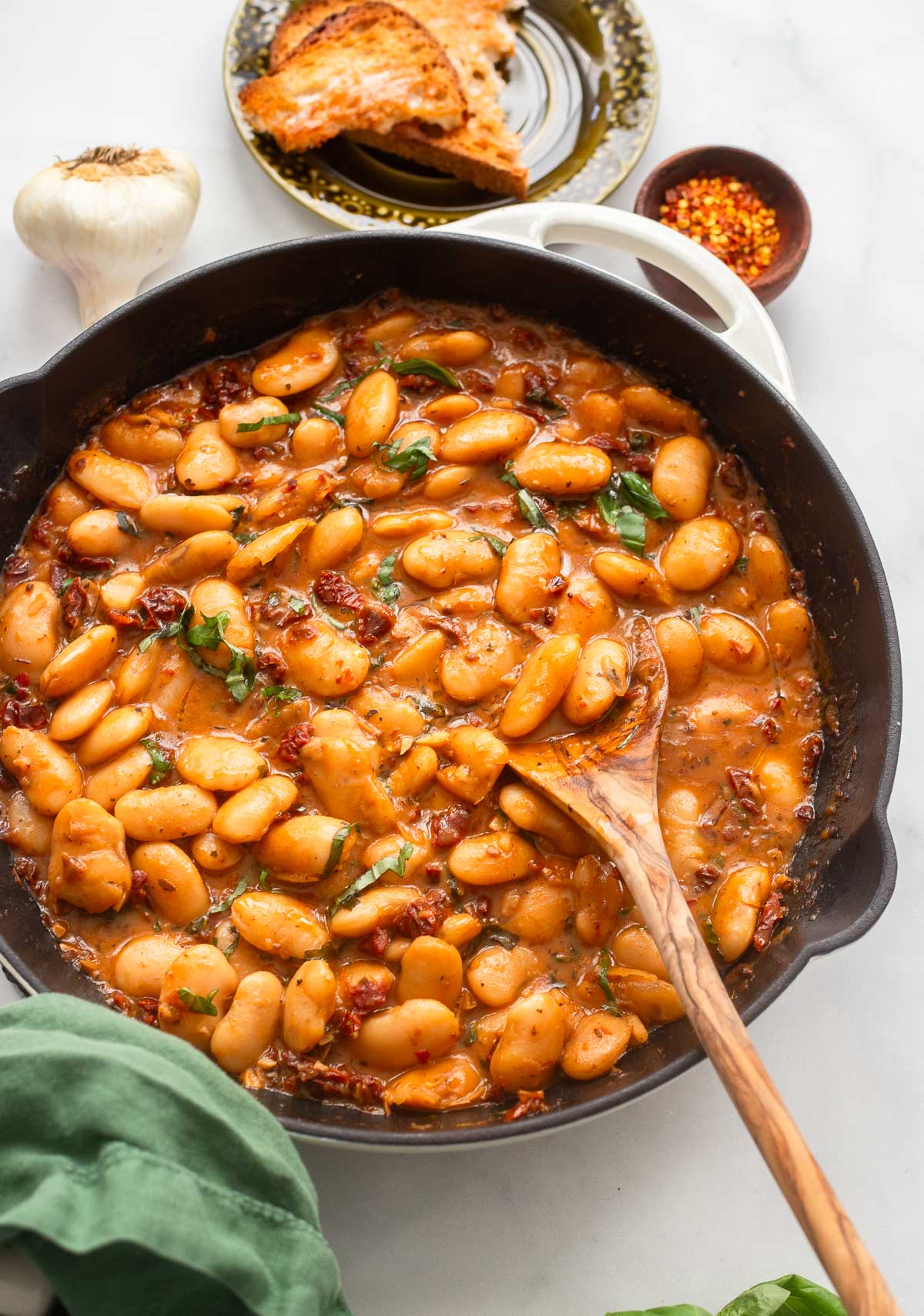 saucy butter beans in an enamelware skillet with a spoon