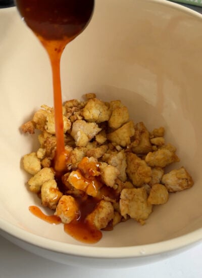 crispy tofu in a bowl with chili sauce poured on top.