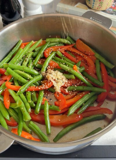 stir fried green beans and red bell pepper in a skillet.