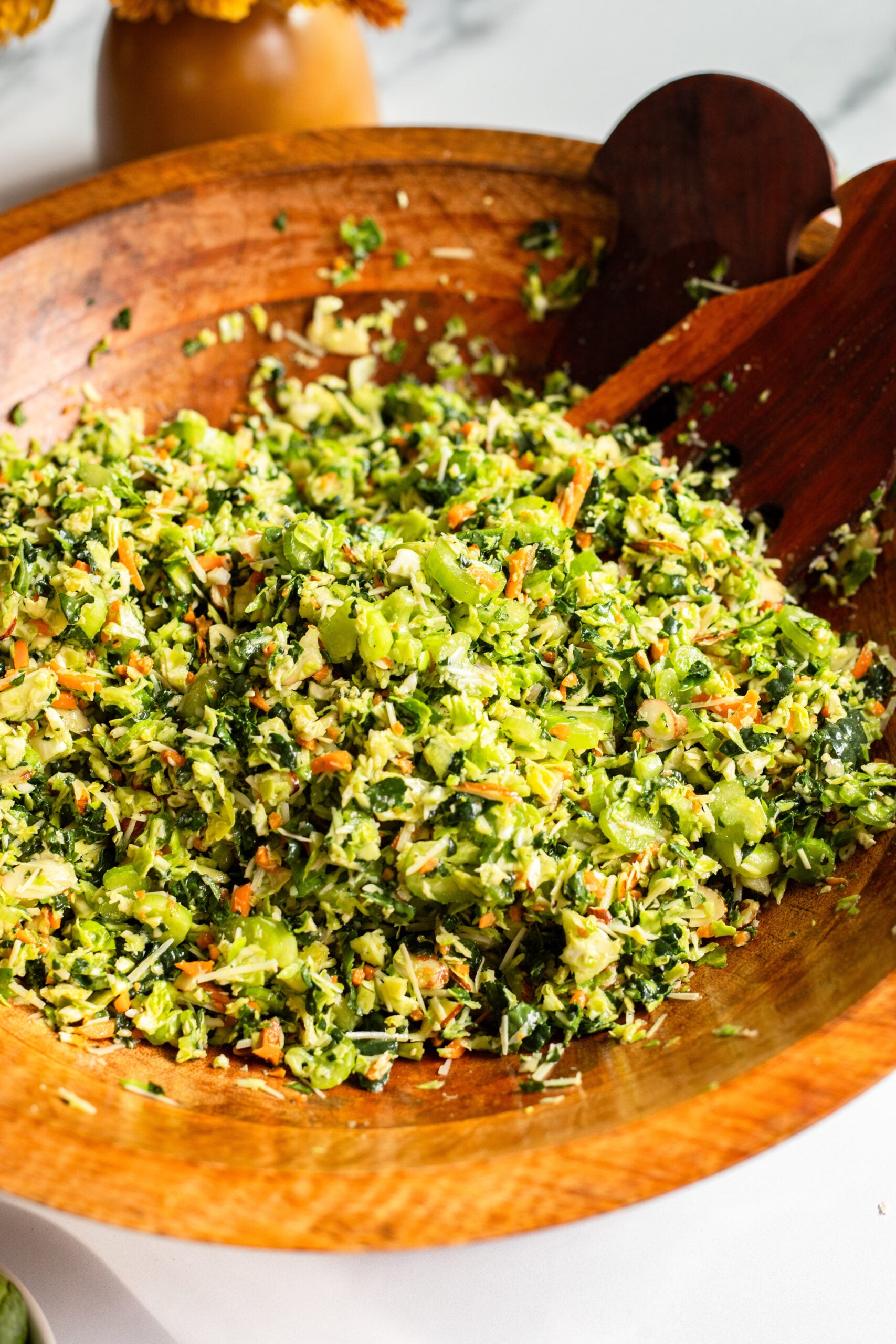 kale, brussels sprouts, and celery slaw in a large wooden serving bowl with utensils