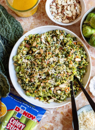 kale brussels sprouts celery slaw in a serving bowl with spoons